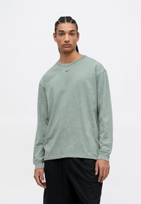 Camică cu mânecă lungă, de culoare verde estompată, cu guler rotund, realizată dintr-un material moale din bumbac; are un mic logo Nike, de culoare neagră, pe piept.