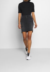 Černý krátký rukávový top spárovaný s tmavě modrou denimovou minisukní s poškozením a třepeným lemem, doplněný bílými teniskami.