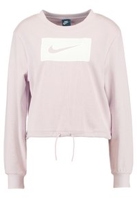 Růžová zkrácená mikina vyrobená z měkké tkaniny. Na přední straně je bílé logo Nike a spodní lem má šňůrku na stažení. Dlouhé rukávy s manžetami.