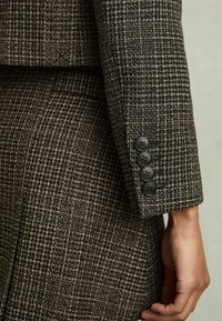 Rukáv hnědé a černé hounds-tooth vzorované bundy s čtyřmi černými knoflíky na manžetě, texturovaná tkanina, upravený design.
