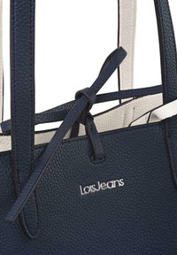 Bolso tote de cuero texturizado azul marino con detalles en cuero blanco. Presenta asas largas y un logotipo plateado en la parte delantera.