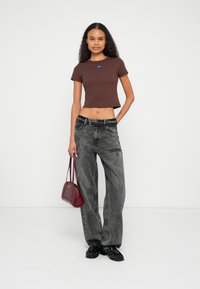 Καφέ κοντό t-shirt, γκρι τζιν με φαρδιά μπατζάκια και φθαρμένες λεπτομέρειες, μαύρα στιλπνά μοκασίνια και μικρή μπουρντόν τσάντα.