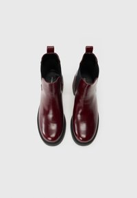 Botas de tornozelo em pele burgundy com um design elegante, painéis laterais elásticos e solas em borracha preta. Inclui uma pega traseira para facilitar o uso.