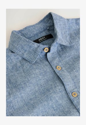 Chemise en lin bleu clair avec un col boutonné, présentant deux boutons beiges et un tissu texturé. L'étiquette indique "NEXT".