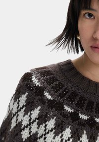 Maglione lavorato a maglia con scollatura rotonda. Base marrone scuro, con motivi geometrici bianchi e grigio chiaro sul petto e sulle spalle.