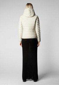 Witte pufferjack met horizontale stiksels en een capuchon, gecombineerd met een lange zwarte geribbelde rok, gezien van achteren.