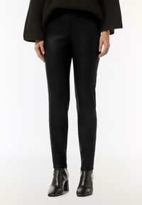 Czarne dopasowane spodnie wykonane z gładkiego materiału, z wysokim stanem i delikatnym połyskiem, w połączeniu z czarnymi botkami na obcasie.