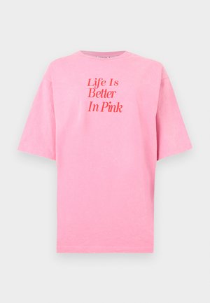 Rožinės spalvos trumpomis rankovėmis marškinėliai su raudona užrašu „Gyvenimas yra geresnis rožinėje“ įrėminti priekyje ant balto fono.