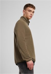 Olivengrønn fleecegenser med høy krage og halv glidelås. Myk tekstur og lange ermer, med en avslappet passform og få sømmer.