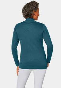 Türkiser gestrickter Pullover mit einem halben Rollkragen, langen Ärmeln und einem gerippten Textur, kombiniert mit weißen Hosen.