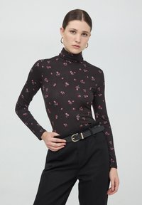 Maglione nero a maniche lunghe con colletto a dolcevita e stampa floreale in rosa e bianco. Abbinato a pantaloni neri a vita alta e una cintura nera con fibbia dorata.