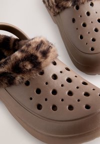 Brown clogs with a textured upper and ventilation holes, featuring a faux fur leopard print trim around the edge.