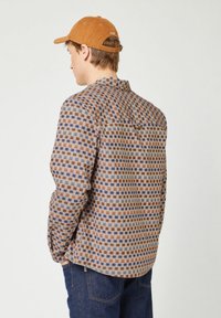 Bruine geruite shirt met blauwe en beige vierkanten, lange mouwen en een kraag, gecombineerd met een bruine corduroy pet. Getextureerde stof.