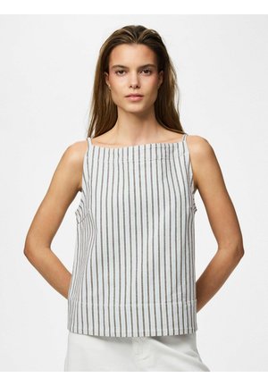 Kvinne iført en hvit ermeløs topp med tynne vertikale brune striper, stående med hendene bak ryggen mot en ensfarget hvit bakgrunn.