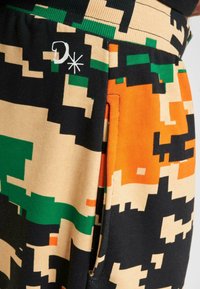 Camouflage-mønstret joggers i orange, grønne og beige farver. Har en sikret lomme og et broderet logo på taljen.