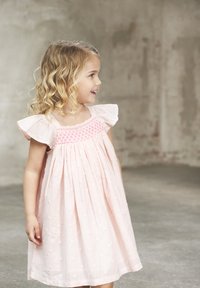 Blassrosa Kleid mit kurzen, fließenden Ärmeln, gerafftem Oberteil mit rosa Stickerei und einem strukturierten Punktmuster auf dem Stoff.