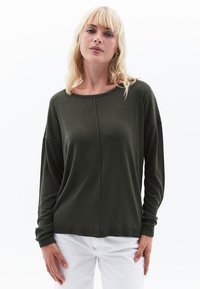 Donkergroene langemouwen top met een relaxte pasvorm, voorzien van een brede halslijn en ribgebreide manchetten, gecombineerd met witte broeken. Mooie, gladde textuur.