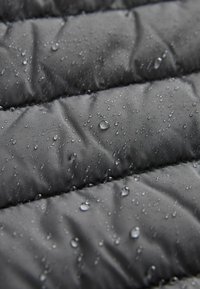 Material puffer negru, rezistent la apă, cu un design matlasat, având picături de apă pe suprafața sa pentru o textură și o protecție îmbunătățite.