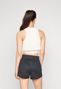 Débardeur blanc court avec un motif texturé, associé à un short noir avec une taille élastique et un ourlet arrondi.