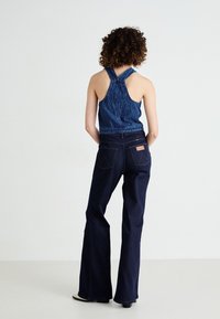 Denim halterica s teksturiranim uzorkom u tamnoplavoj boji, u kombinaciji s raširenim tamnoplavim trapericama koje imaju kožnu oznaku i dvostruke stražnje džepove.