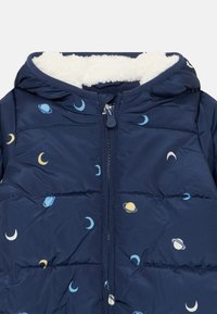 Casaco acolchoado azul-marinho com capuz, apresentando um forro branco macio, fecho com zíper e estampas celestiais coloridas de planetas e luas.