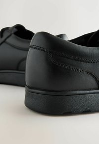 Chaussures en cuir noir avec une texture lisse, bout arrondi et détails de couture sur le côté. Elles disposent d'une semelle épaisse en caoutchouc noir texturé.
