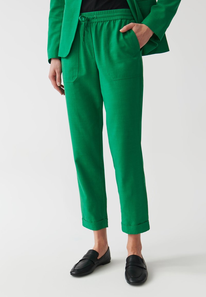 Groene, lichte broek met een elastische tailleband, twee zijzakken en opgerolde mouwen. Gecombineerd met zwarte loafers, wat een ontspannen pasvorm laat zien.