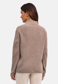 Brązowy sweter z prążkowanego dzianiny z wysokim kołnierzem, luźnym krojem i długimi rękawami. Teksturowana tkanina o miękkim wyglądzie.