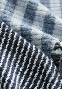 Stickad tyg med blå, vit och marinrandiga mönster; texturerat mönster med en distinkt lurvig ytfinish; inkluderar broderad detalj i hörnet.