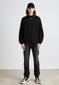 Black long-sleeve sweatshirt with a small white logo, paired with dark jeans and black and white sporty shoes, featuring a smooth texture.