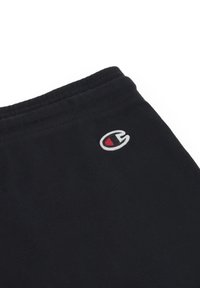 Zwarte sweatpants met een elastische tailleband, voorzien van een klein geborduurd logo in wit en rood aan de linkerkant. Zachte katoenmateriaal structuur.