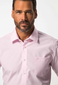 Camicetta rosa chiaro con colletto classico, chiusura a bottoni e taschino con logo ricamato "JP". Tessuto liscio e vestibilità su misura.