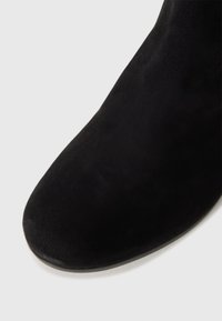 Schwarze Wildleder-Stiefelette mit runder Zehenform, die eine schlanke Silhouette und eine glatte Textur aufweist. Minimalistisches Design ohne sichtbare Beschläge.