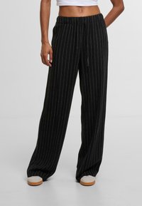 Široké nohavice v čiernej farbe s bielym pruhovaním, s elastickým pásom a šnúrkou na stiahnutie, vyrobené z textúrovanej tkaniny.