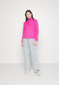 Fuksiaed tagune kaelus-sweater, millel on soonikstruktuur, koos helesiniste laiadest jalgadest teksade ja hallide tossudega.