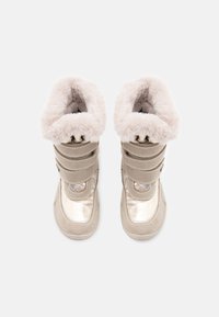 Botas impermeáveis bege com colarinho de pelúcia sintética, fechos em tiras de velcro, detalhes em prata brilhante e parte superior texturizada. Forro interno suave visível.