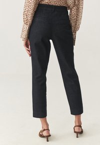 Temno modri traper hlače z oprijetim krojem, skrajšano dolžino in dvema zadnjima žepoma. Gladka tekstura, brez vidnih vzorcev, v kombinaciji z rjavimi petami.