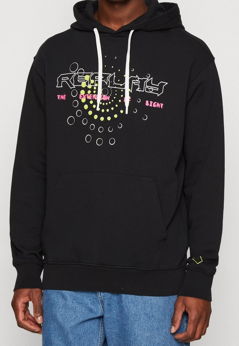 Sweat à capuche noir avec cordons blancs et poche devant, présentant un design circulaire abstrait et un texte en blanc, rose et jaune sur la poitrine.