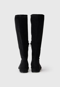 Botas pretas até ao joelho, feitas de camurça, com uma textura suave, um ligeiro salto e fechos laterais para facilitar o calçar. Design simples e elegante.