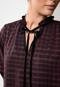 Burgundia läbipaistev pluus tekstuurse ruudustikuga, millel on volangiline krae ja must sametist nöör kaelusel.