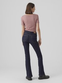 Smal passform, marineblå denimjeans med utsvakt ben, fem-lommers design, og brun lærmerke i livet, brukt med en rosa tettsittende t-skjorte.