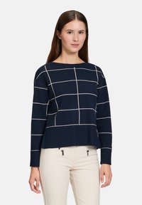 Navy Pullover mit cropped Design, versehen mit cremfarbenen Gitterlinien auf der Vorderseite und geripptem Saum. Hergestellt aus weichem Strickstoff.