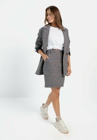 Grauer und mehrfarbig karierter Blazer, kombiniert mit einem passenden Bleistiftrock, getragen über einem weißen, geknoteten T-Shirt und mit hellen Sneakers.