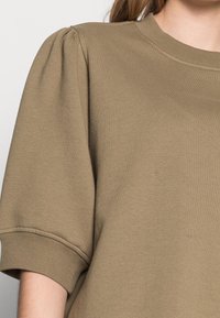 Olivově zelená oversized mikina s kulatým výstřihem, nařasenými krátkými rukávy a žebrovanými detaily na manžetách. Hladký bavlněný materiál.