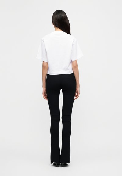 Άσπρο κοντό t-shirt με κοντά μανίκια, σε συνδυασμό με εφαρμοστά μαύρα παντελόνια με καμπάνα. Λείο βαμβακερό ύφασμα, απλός σχεδιασμός χωρίς σχέδια.