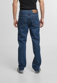Blugi din denim albastru cu un design drept, o etichetă din piele la talie și două buzunare spate cu o textură ușor spălată.