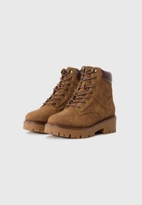 Bottines en suede marron avec une semelle épaisse, un laçage à l'avant et des œillets en métal. Avec des accents en cuir marron au niveau du col.