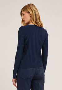 Granatowy sweter rypsowy z długimi rękawami i okrągłym dekoltem, z dopasowanym stanem i textured wzorem. Stylizowany z ciemnymi spodniami.