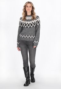 Grauer Strickpullover mit schwarz-weißen Zickzackmustern, kombiniert mit grauen Jeans und knielangen schwarzen Lederstiefeln.