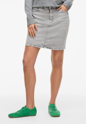 Denim skirt in light gray, knee-length, with a subtle texture and five-pocket design. Paired with green suede sneakers.